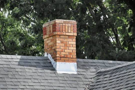 Older brick chimney with decorative top courses and metal flashing among trees